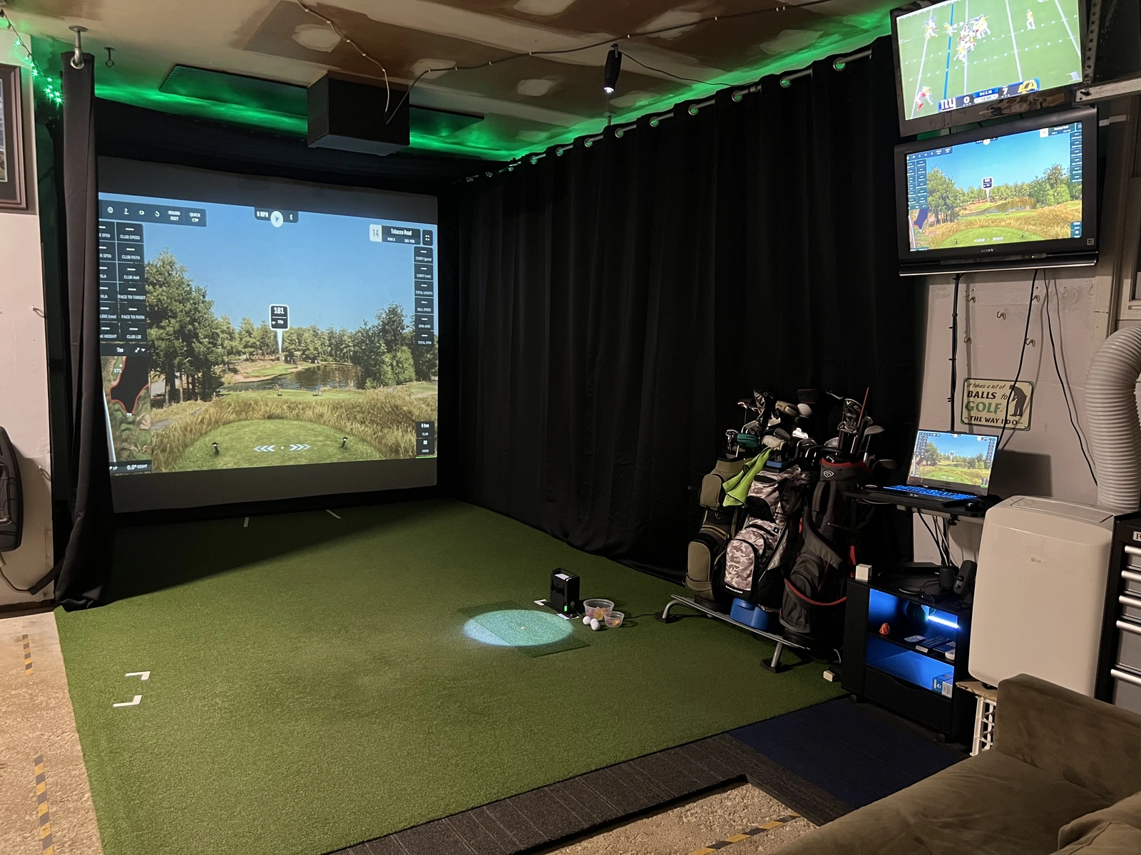 Completed St. Charles garage golf simulator with a screen, turf, black curtains, green lighting, golf bags, televisions, and an unfinished ceiling